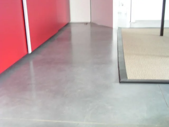 Grijs naturel beton langs een rode wand en een glazen scheiding