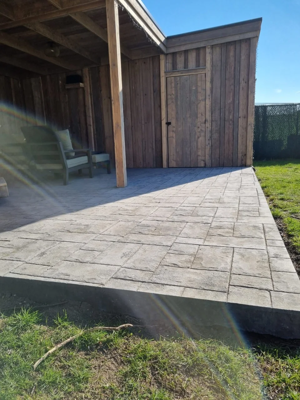 Voorbeeld van een terras in printbeton met een gestempeld steenpatroon bij een houten bijgebouw