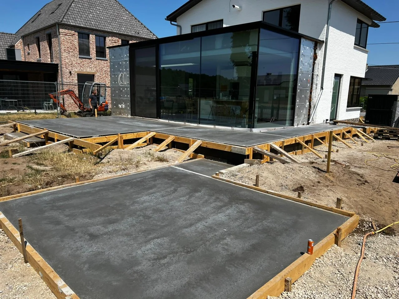 Overzicht van het betonterras rond de woning met houten randbekisting en schoren