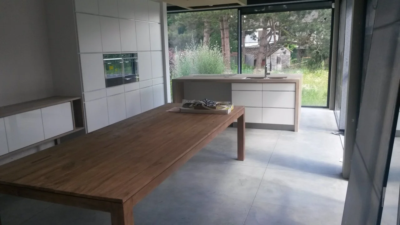 Grijze betonvloer bij een houten eettafel en witte keuken