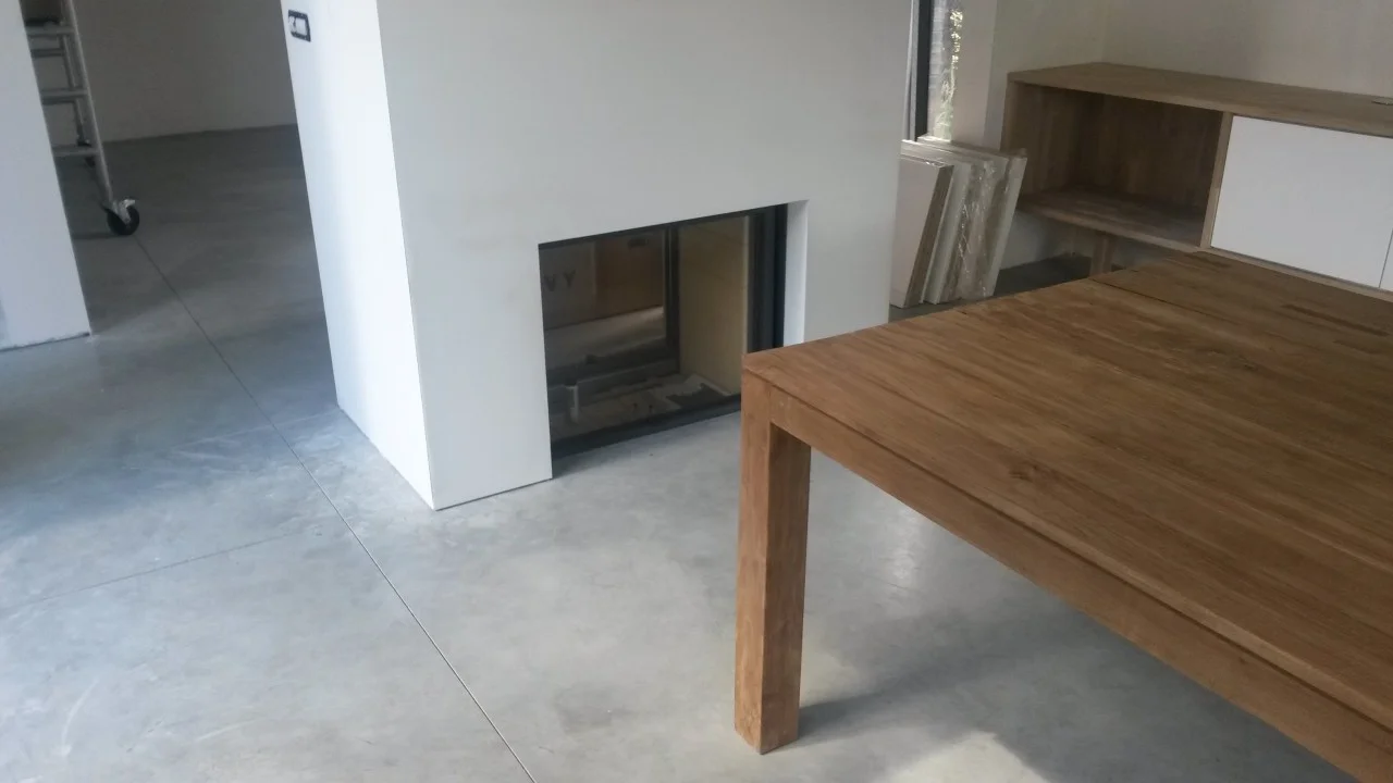 Kleurnuances en voegen in een betonvloer bij een haard en houten tafel